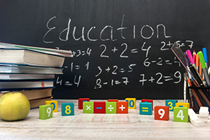 Green apple with stack of books and writing supplies against blackboard. Education concept