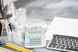 photo of a microscope, beakers, calculator and keyboard sitting on a desk