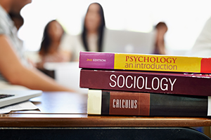 photo of psychology, sociology, and calculus textbooks stacked on a desk
